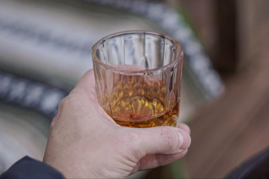 少量のウイスキーが入ったグラスを持つ男性の左手
