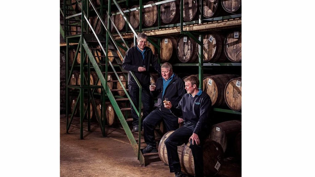 スキャパ蒸溜所で厳守を造りだすクラフトマンが、樽の並んだ倉庫でウイスキーをテイスティングしている