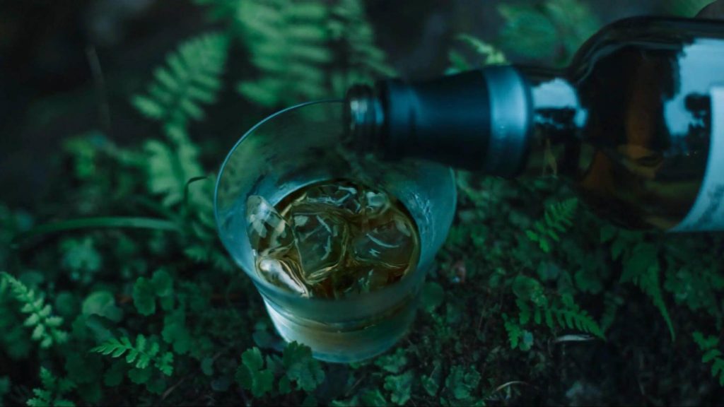 自然の中で氷の入ったグラスに戸河内ウイスキーを注ぐ様子